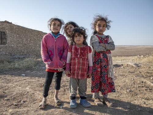Four young children stand near their damaged home while looking straight up at the camera.