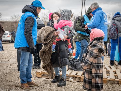 A group of people wrapped in winter clothing talk to UNHCR staff.