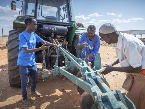 Three people work on machinery attached to a tractor.