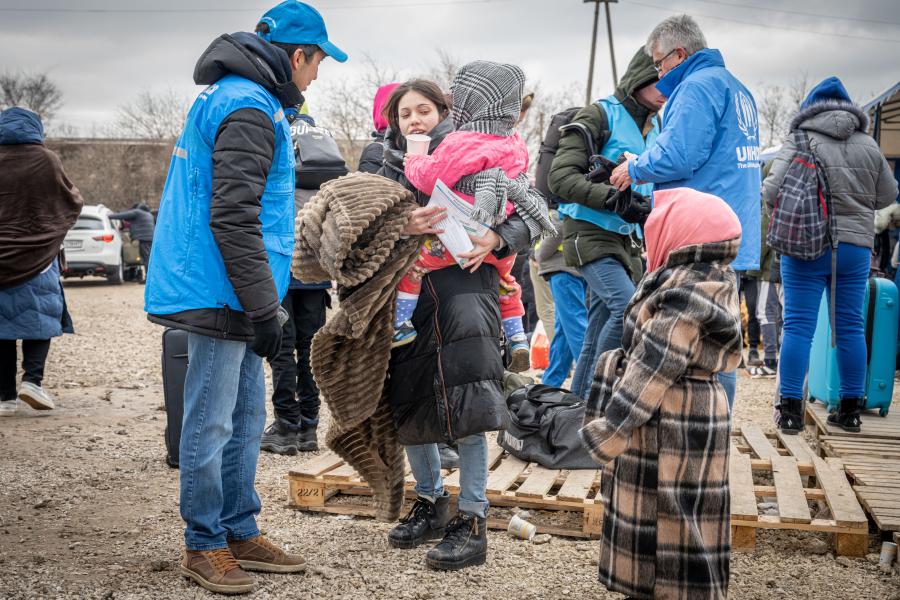 A group of people wrapped in winter clothing talk to UNHCR staff.