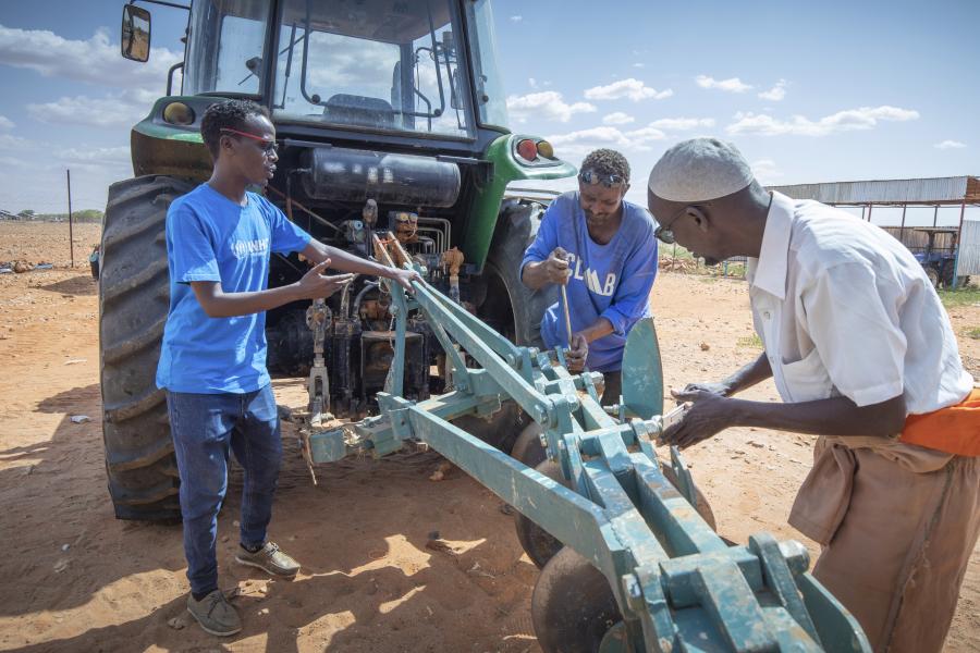 Three people work on machinery attached to a tractor.