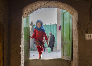 A young and joyful girl dressed in red runs down the stairs of a settlement for displaced people.