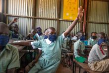 A 13-year-old girl raises her hand in a Kenyan classroom.