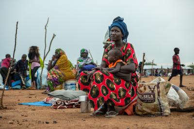 A woman sitting while carrying her baby in her arms. 