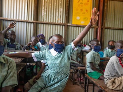 A 13-year-old girl raises her hand in a Kenyan classroom.