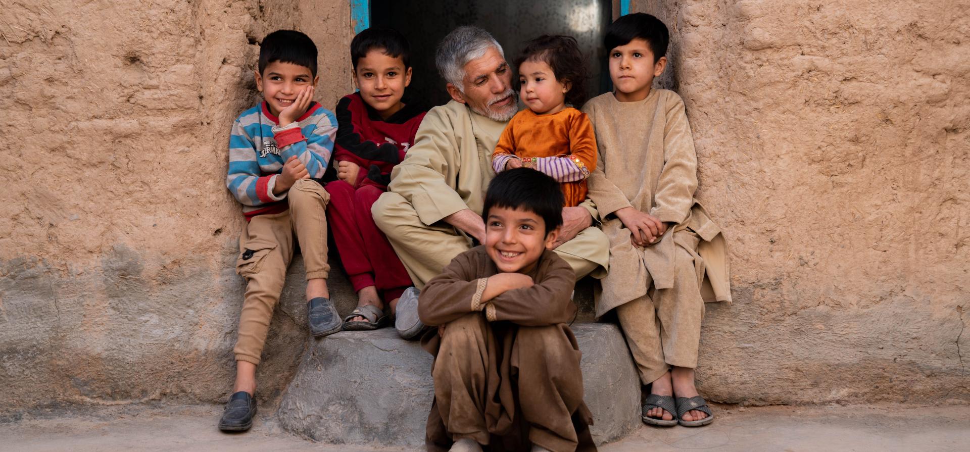 man sitting on a door step surrounded by kids