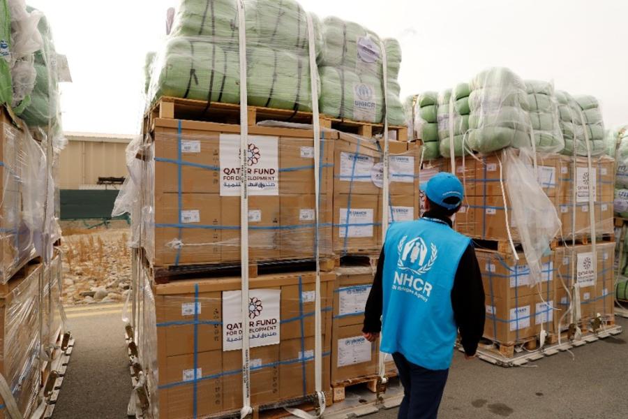 A man in a UNHCR vest looking at cartons 
