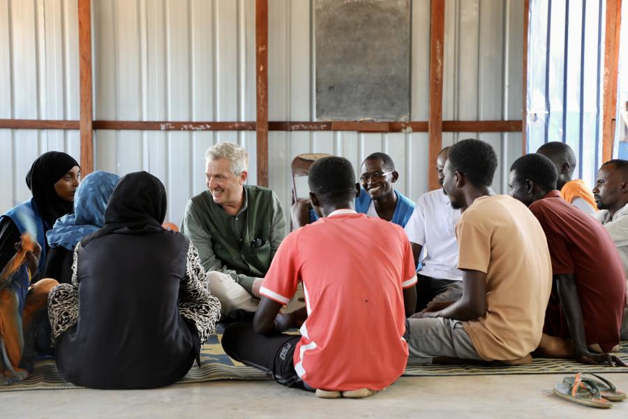 High Commissioner siting down on the ground with with a group of young Sudanese refugees 