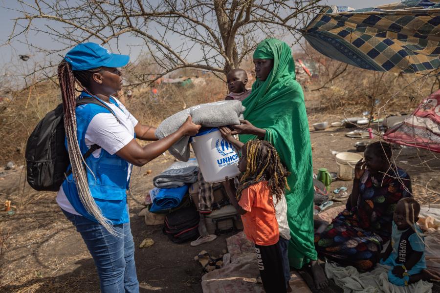 UNHCR Associate Child Protection Officer Lilian Sabasi, hands over core relief items, including blankets, mats and a bucket, to Achan, a mother-of-six, at her shelter in the bush near the UNHCR transit centre in Renk, South Sudan. 