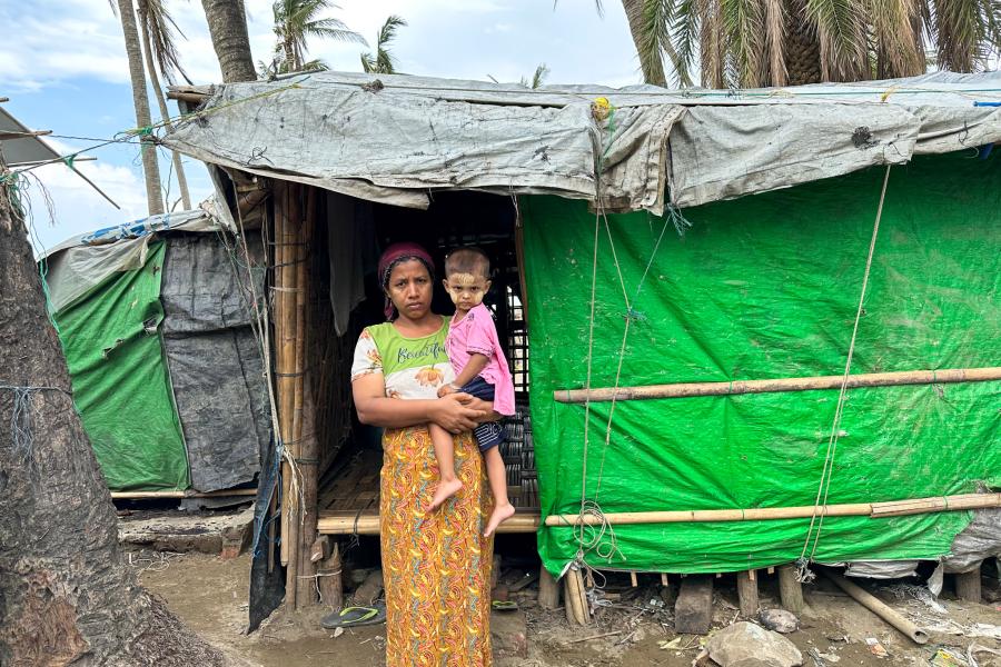 A woman standing with her child Infront of a makeshift shelter. 