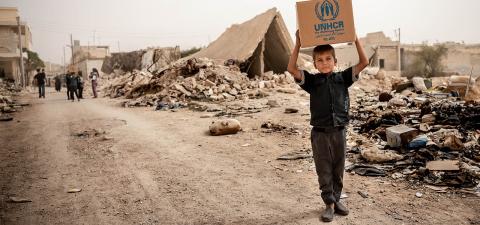 A young boy carrying a box full of supplies provided by UNHCR.