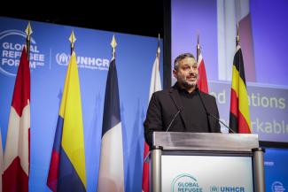 person speaking at podium with flags behind